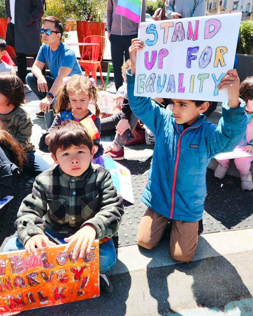 Students hold up signs on Harvey Milk Day that read "stand up for equality" and "we love Harvey Milk."